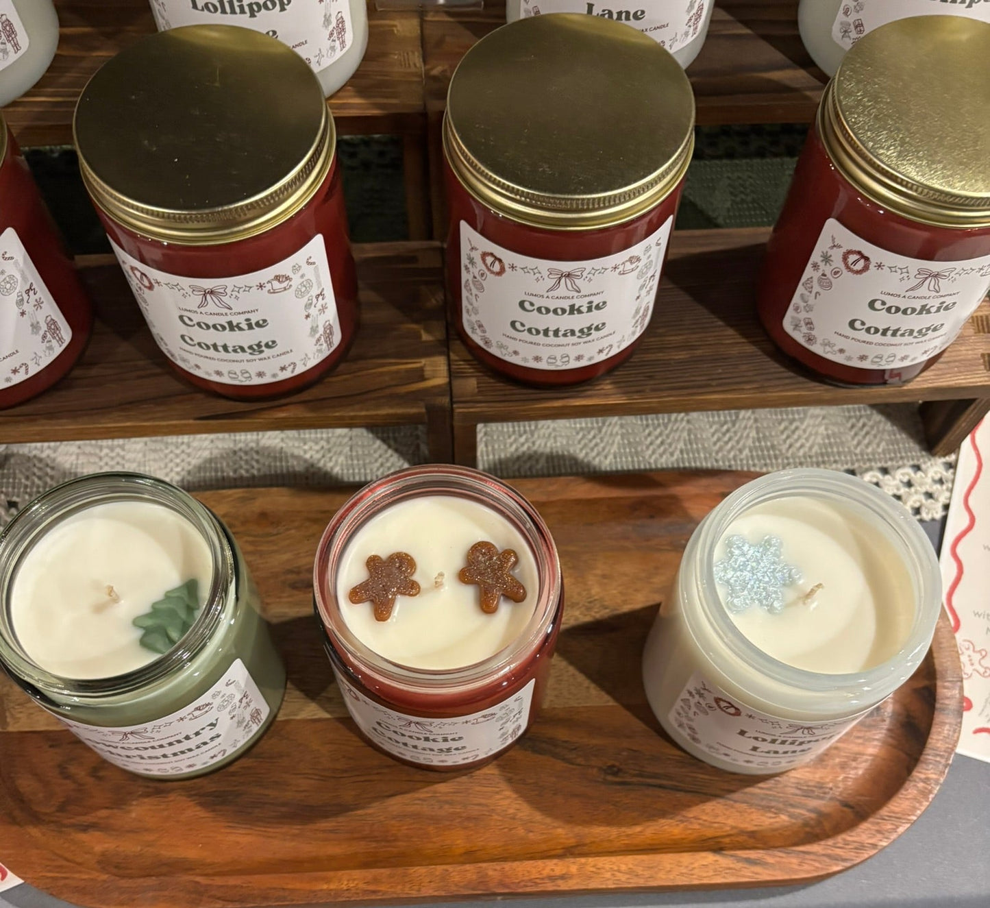 Jars of candles with visible labels on a wooden shelf.