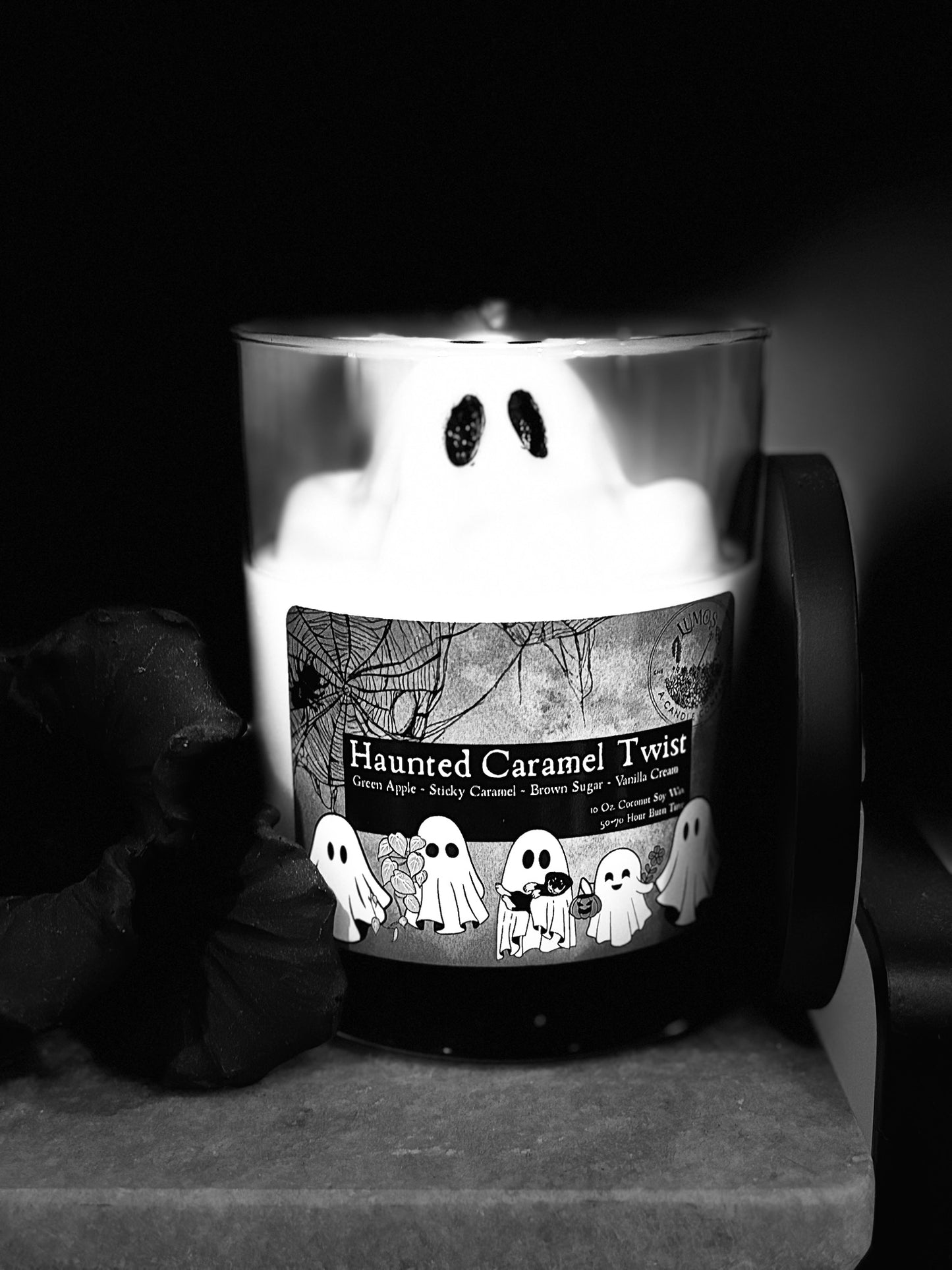 Candle with a label featuring ghosts and the name 'Haunted Caramel Twist' on a dark background.