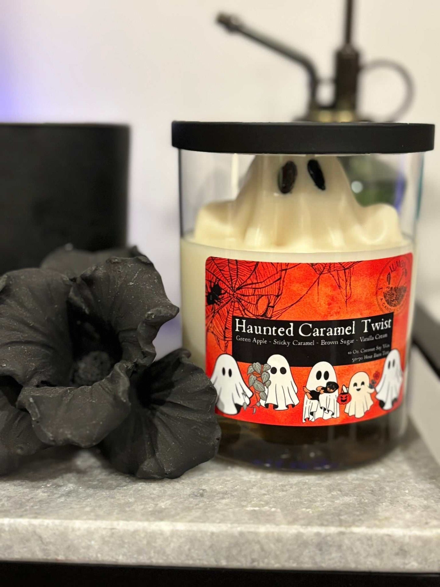 Candle labeled 'Haunted Caramel Twist' with ghost design on a dark surface