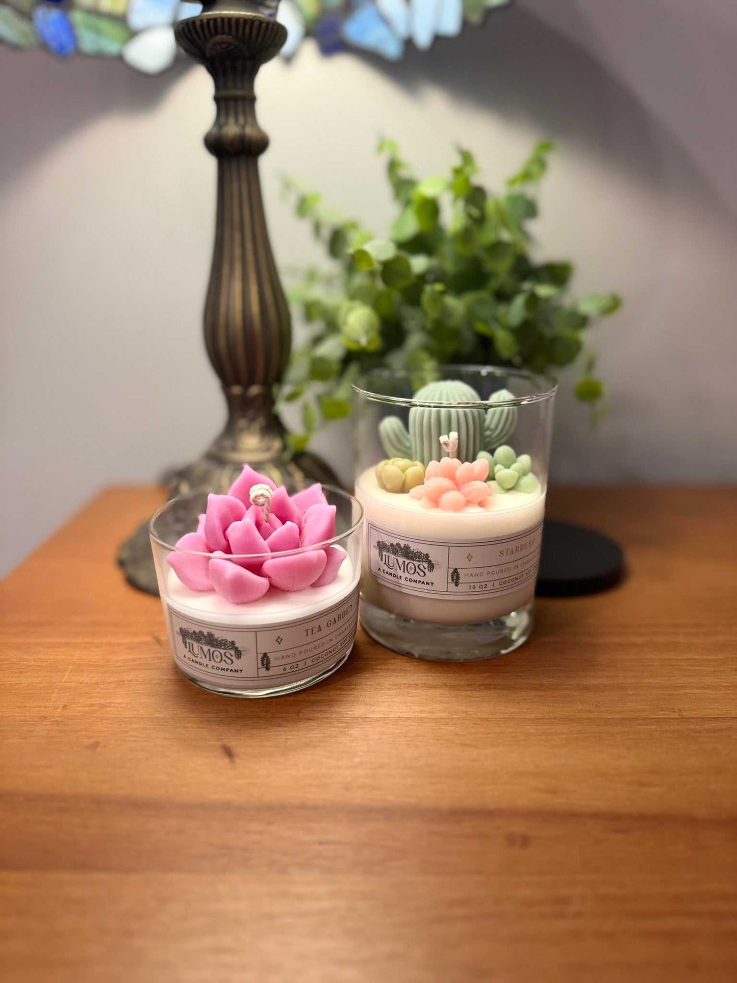 Two small glass containers with decorative plant-like figures on a wooden surface.