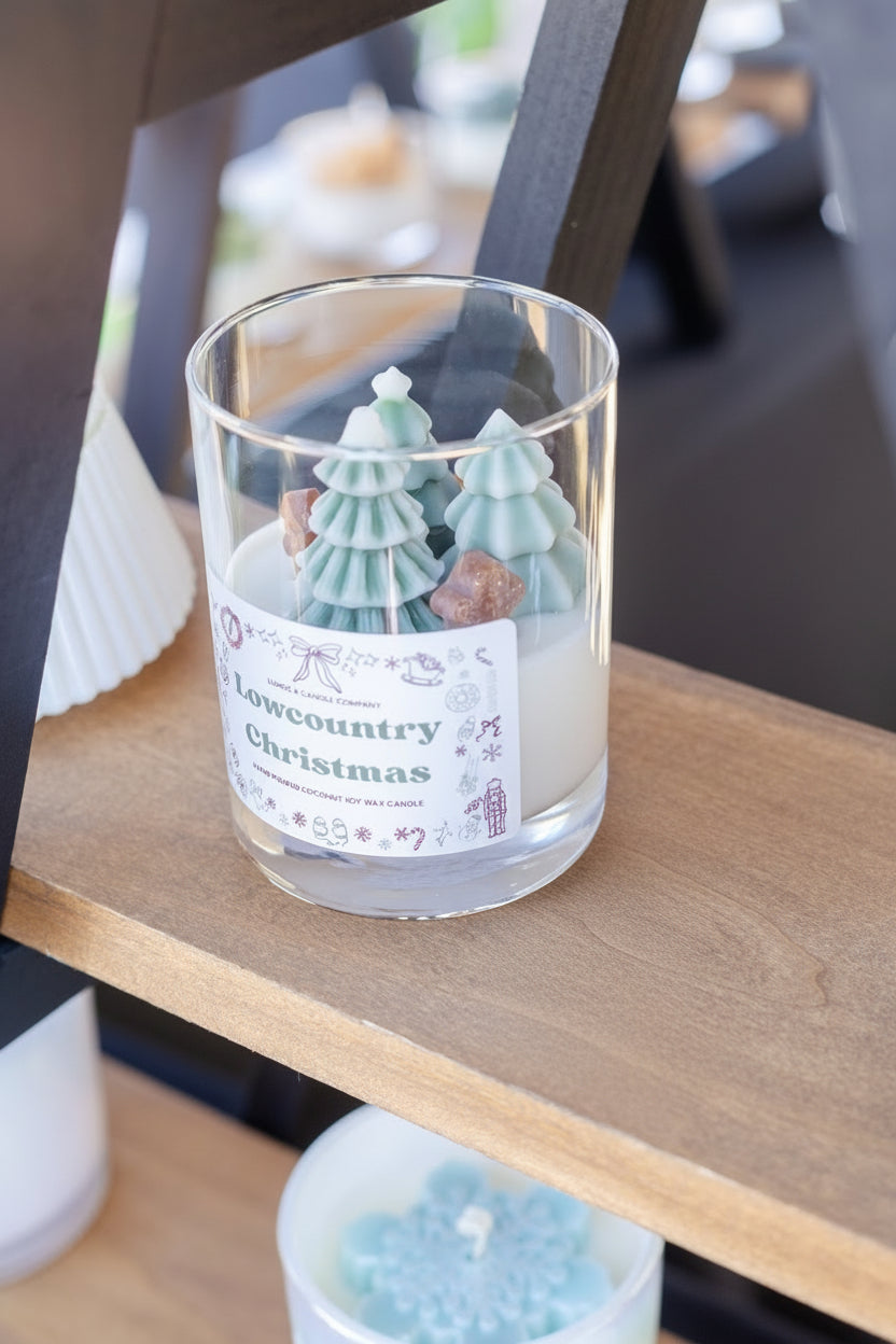 Glass candle with decorative trees on a wooden surface