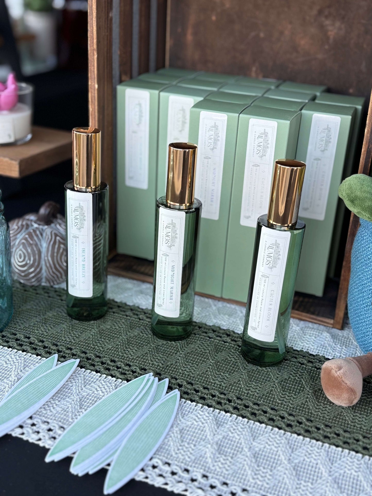 LUMOS Room + Linen Spray luxury home fragrance mist in elegant green bottles with gold caps displayed with matching green packaging
