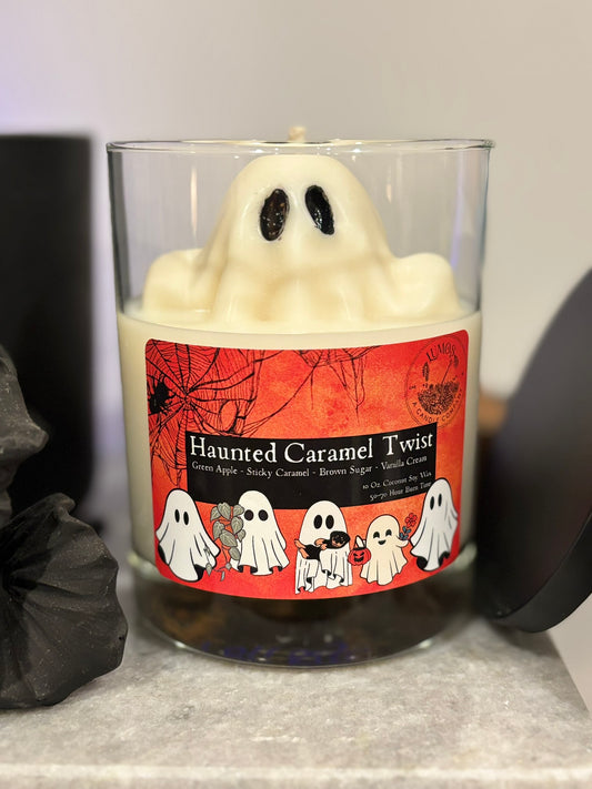 Halloween-themed candle with ghost design and 'Haunted Caramel Twist' label on a gray surface.