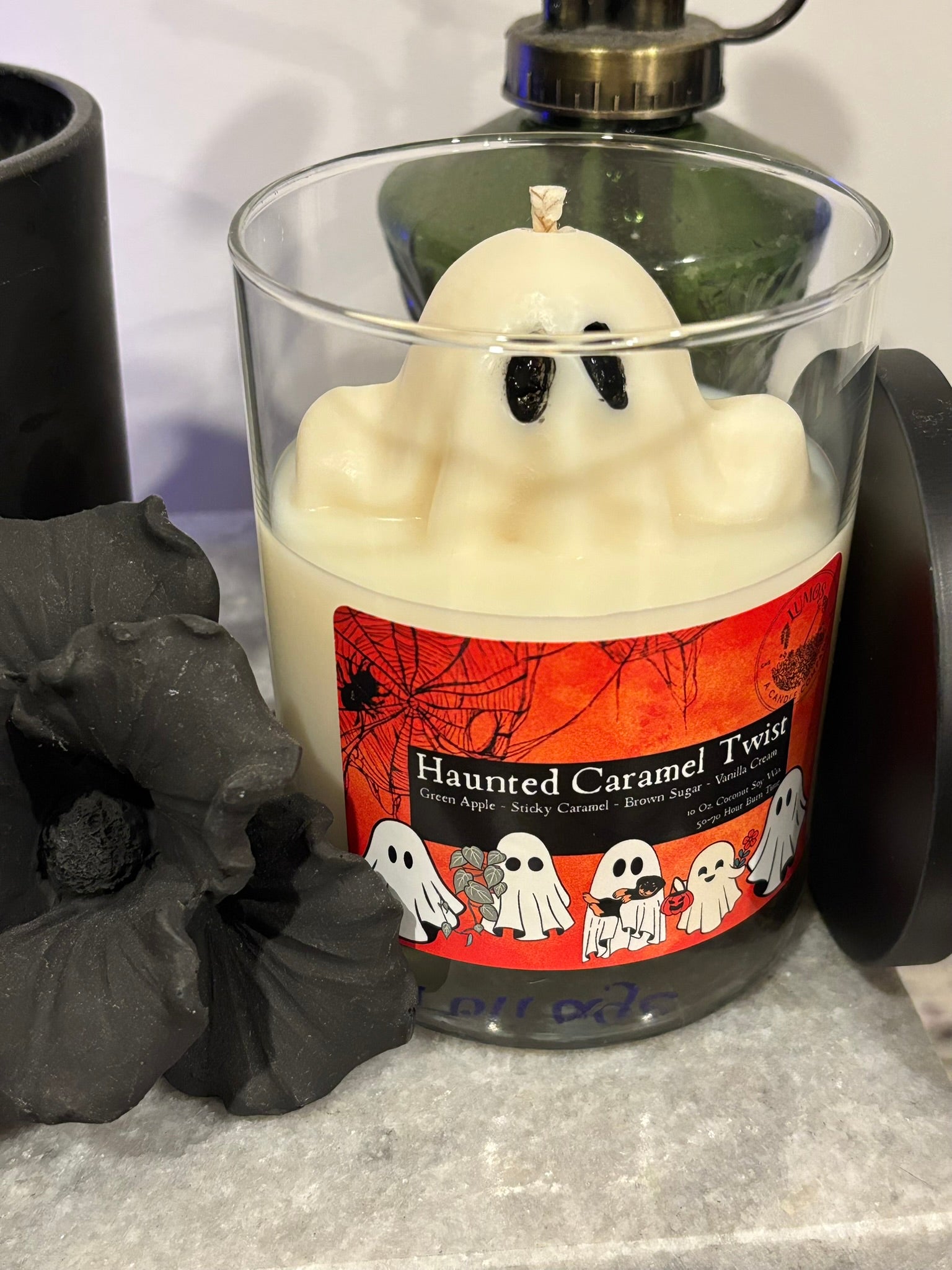 Ghost-shaped candle with a Halloween-themed label on a gray surface.