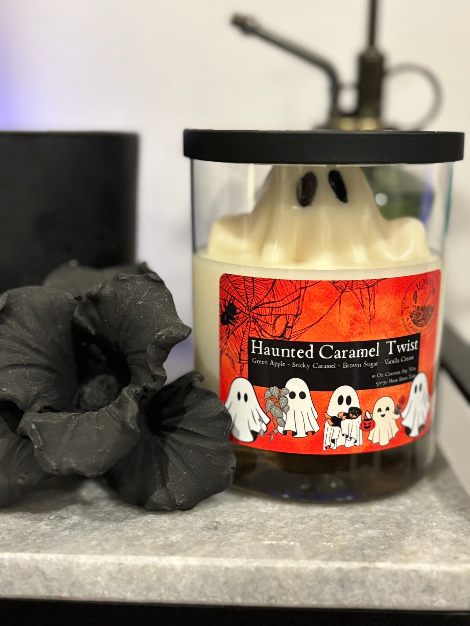 Candle labeled 'Haunted Caramel Twist' with ghost design on a dark surface