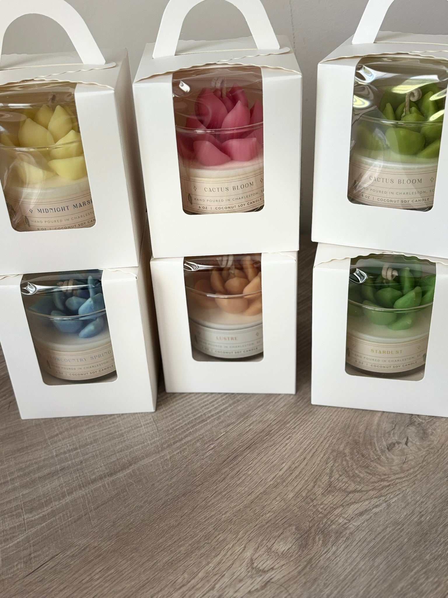 Succulent terrarium candles in multiple colors packaged in white boxes with handles on a wooden surface
