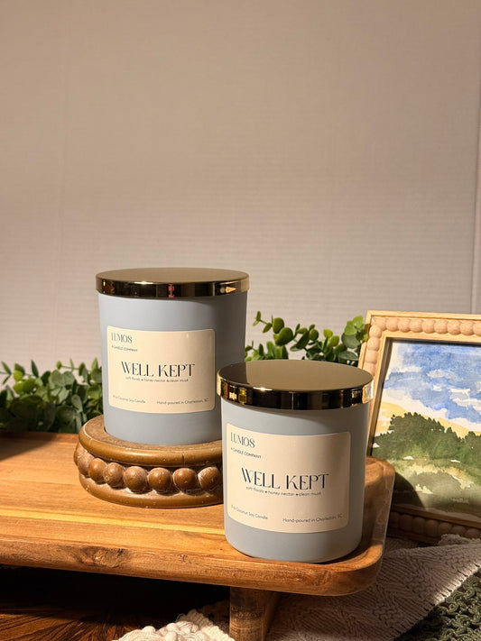 Well Kept candle in a matte blue glass vessel with a gold lid, cream label, and single wick.
