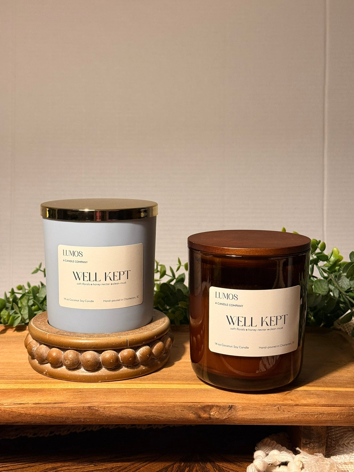 Well Kept candle in a matte blue glass vessel with a gold lid and cream label, beside an amber glass version.